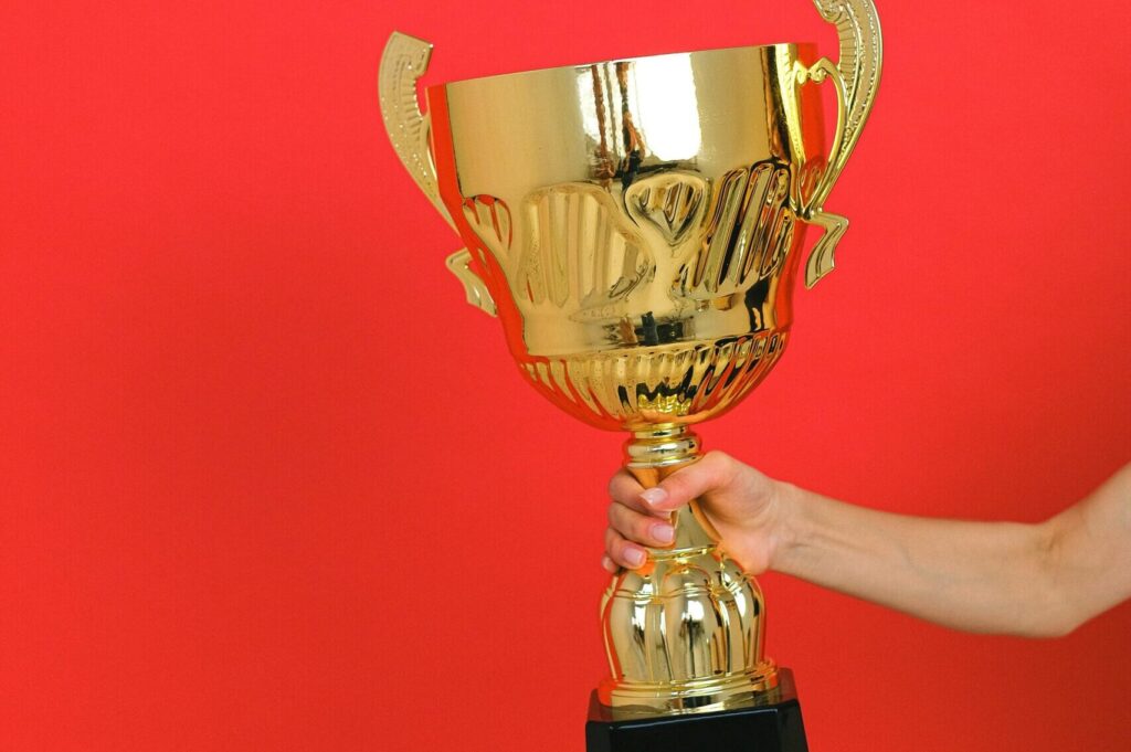 Close-up of a hand holding a gold trophy against a bold red background.